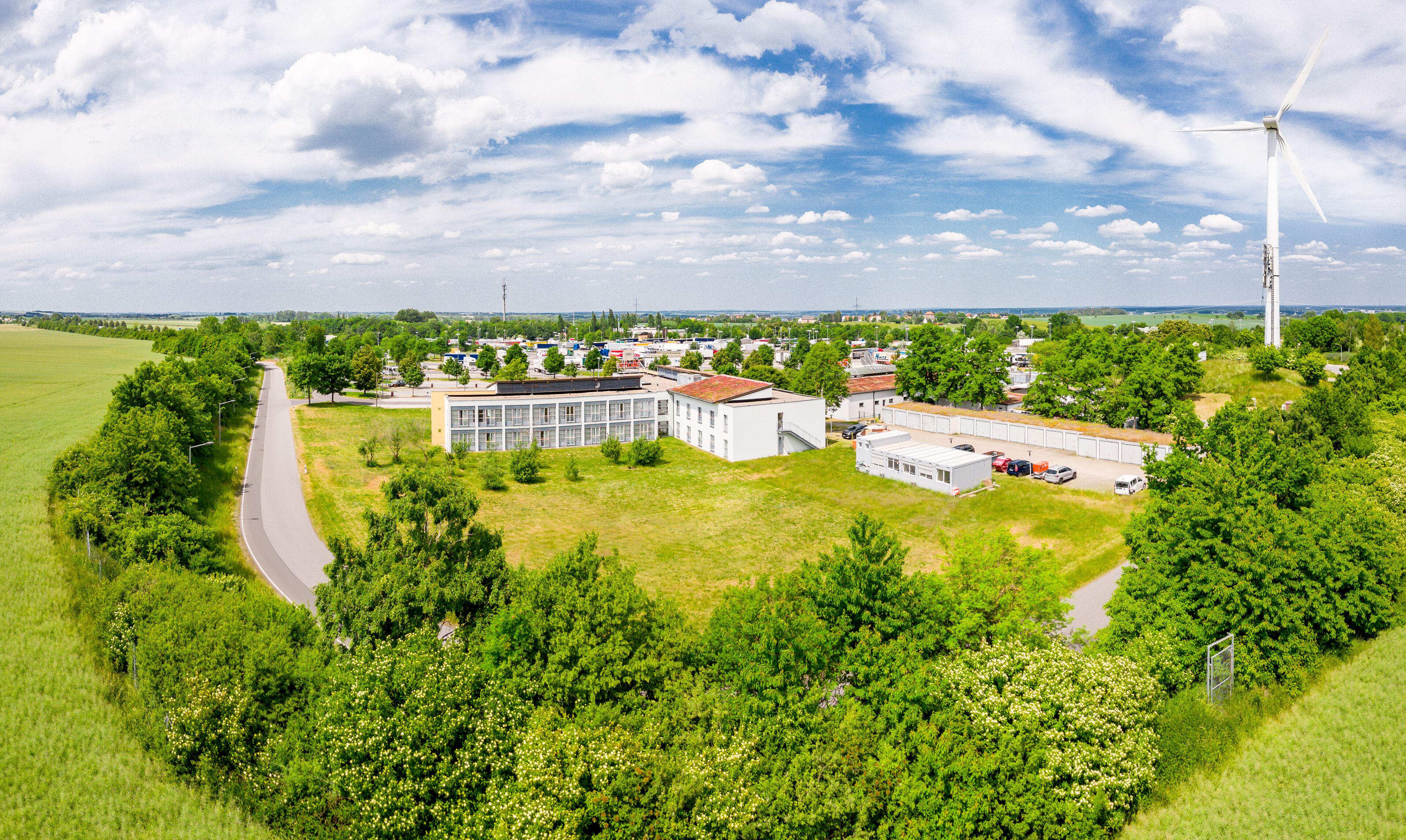 A rural area with a large building complex, a road, and a wind turbine.