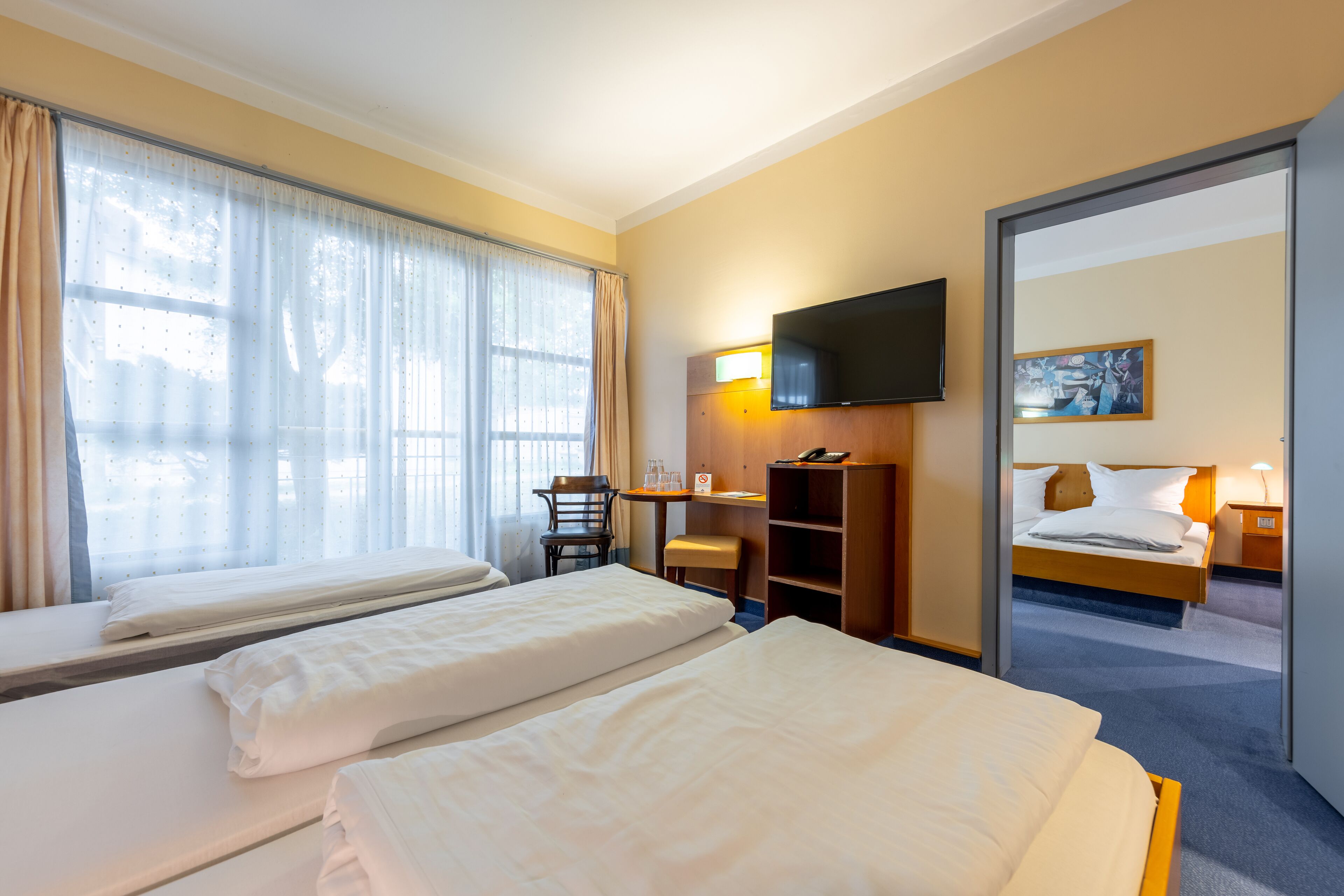 Ein Hotelzimmer mit zwei Betten, einem Schreibtisch, einem Sessel, einem Fernseher und einem Bild an der Wand.
