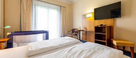 Ein Hotelzimmer mit zwei Betten, einem Schreibtisch, einem Stuhl, einem Fernseher und einem Fenster mit Vorhängen.
