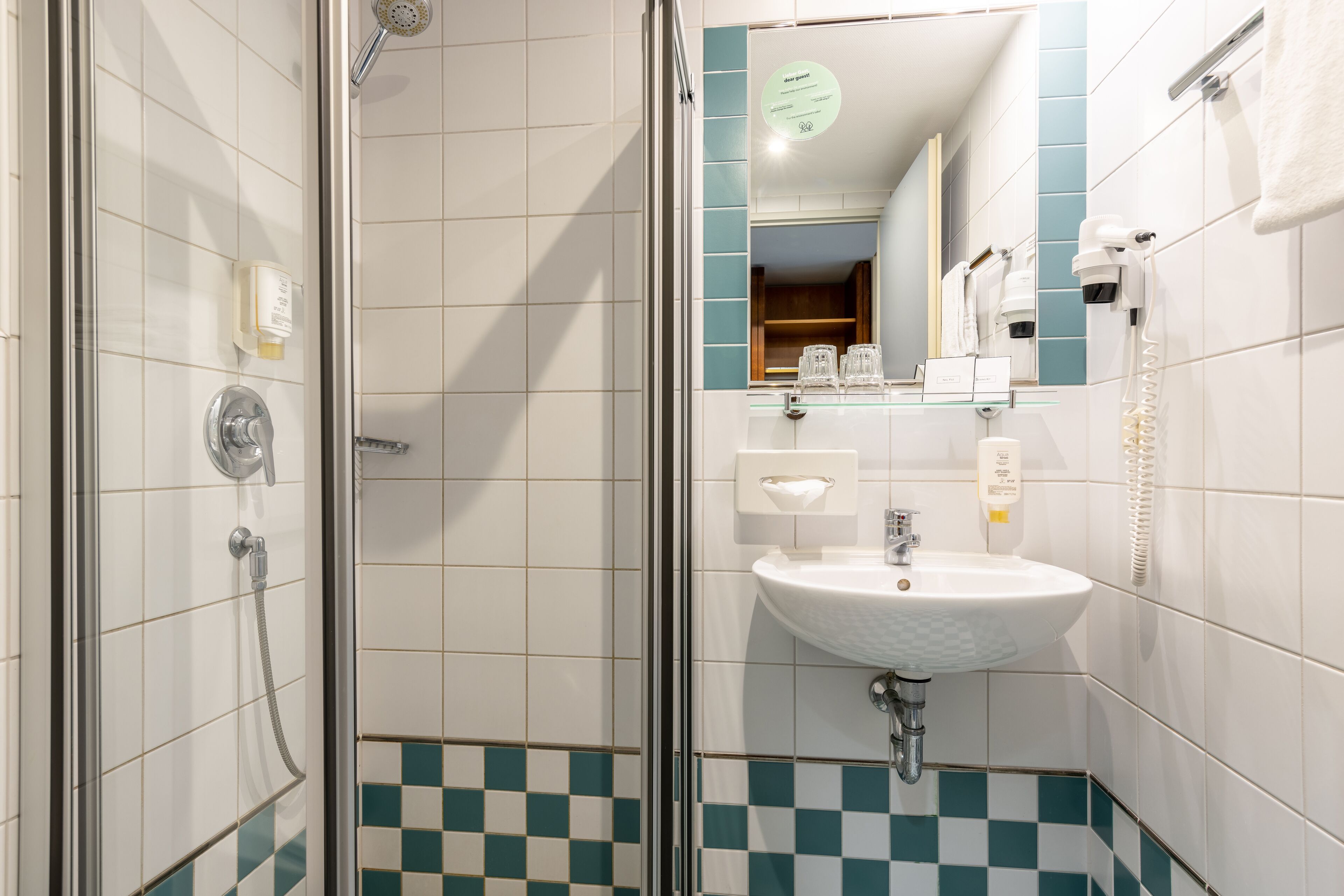 Un baño moderno con ducha de vidrio, un lavamanos blanco y un espejo con zócalo de azulejos azules.