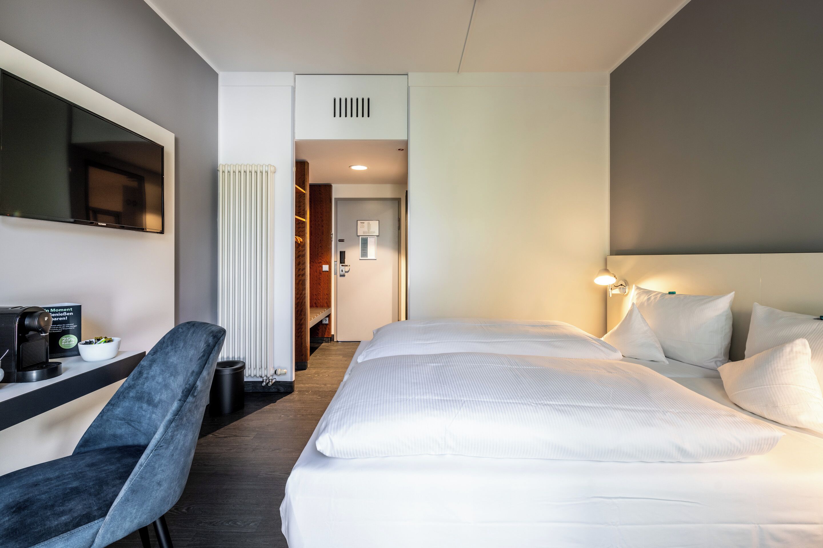 Une chambre d’hôtel équipée d’un lit, d’un bureau avec une machine à café, d’une chaise et d’un téléviseur fixé au mur.