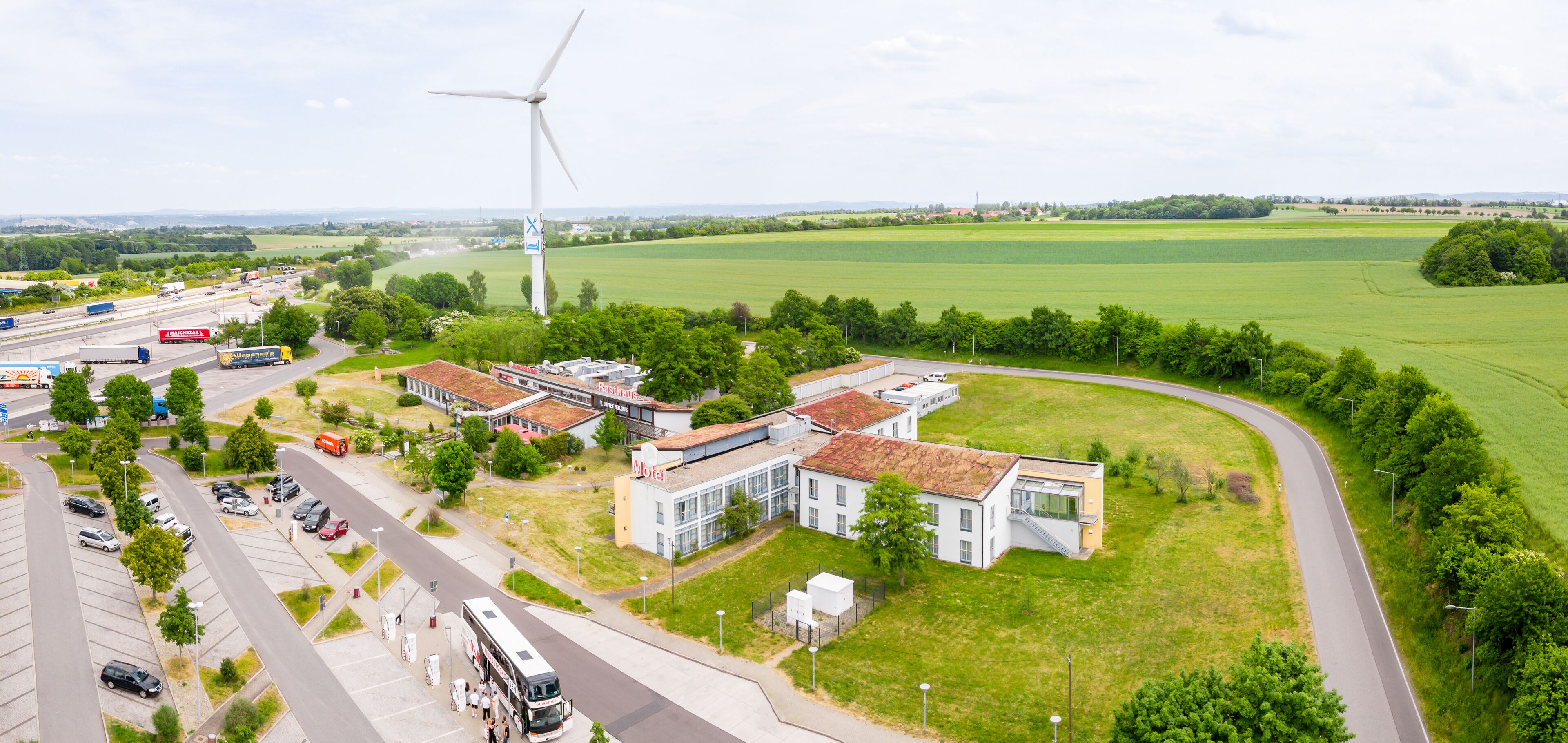 A hotel with a modern design, located near a highway and a large green field.