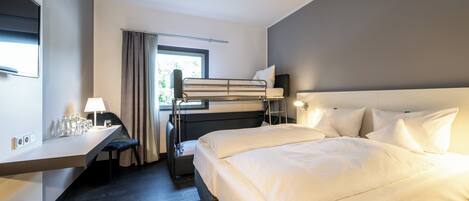 A modern hotel room with a bunk bed, a desk with a lamp, and a large window with curtains.