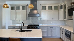 Una cocina moderna con gabinetes blancos, una isla central, una estufa e iluminación colgante.