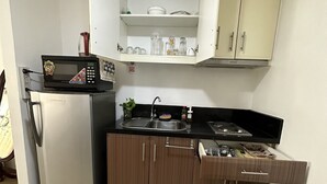 Een kleine keuken met een koelkast, magnetron, spoelbak en houten keukenkastjes.