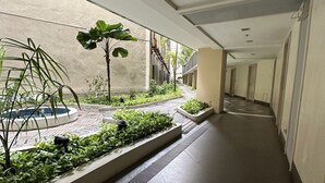 Een gang met een centraal gelegen tuin, een vluchttrap en een betegelde vloer.