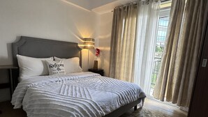 Een slaapkamer met een bed, nachtkastje, lamp en raam met gordijnen.