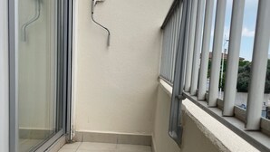 Un balcón con puerta de cristal, pared blanca y barandilla de metal.