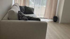 Una sala de estar moderna con un sofá color beige, cojines estampados, cortinas translúcidas y vistas amplias a través de grandes ventanales.