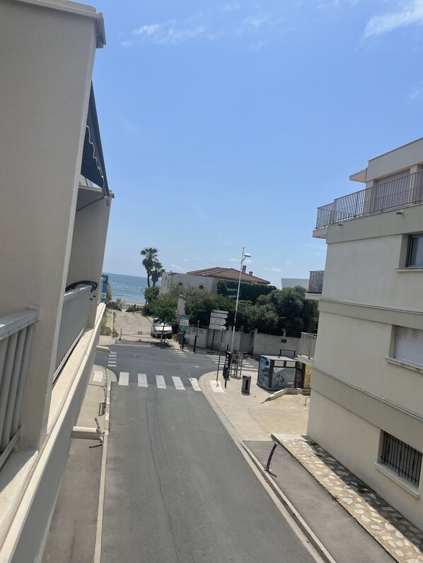 Une vue de rue avec un ciel dégagé, une route avec un passage piéton et des immeubles dotés de balcons.