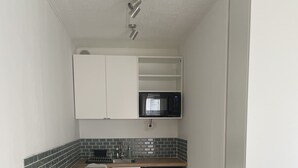Una cocina compacta con armarios blancos, un microondas, un lavavajillas y un revoque de azulejos.