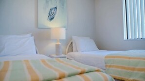 Habitación de hotel con dos camas, una mesita de noche con lámpara, un cuadro en la pared y una ventana con persianas.