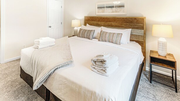 A neatly made bed with a wooden headboard, two bedside lamps, and a framed artwork above it. - King Bed + Walking Distance to Forsyth Park by Lucky Savannah (Savannah)