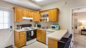 A compact kitchen with wooden cabinets, a stove, a microwave, and a small dining area with two chairs. - King Bed + Walking Distance to Forsyth Park by Lucky Savannah (Savannah)