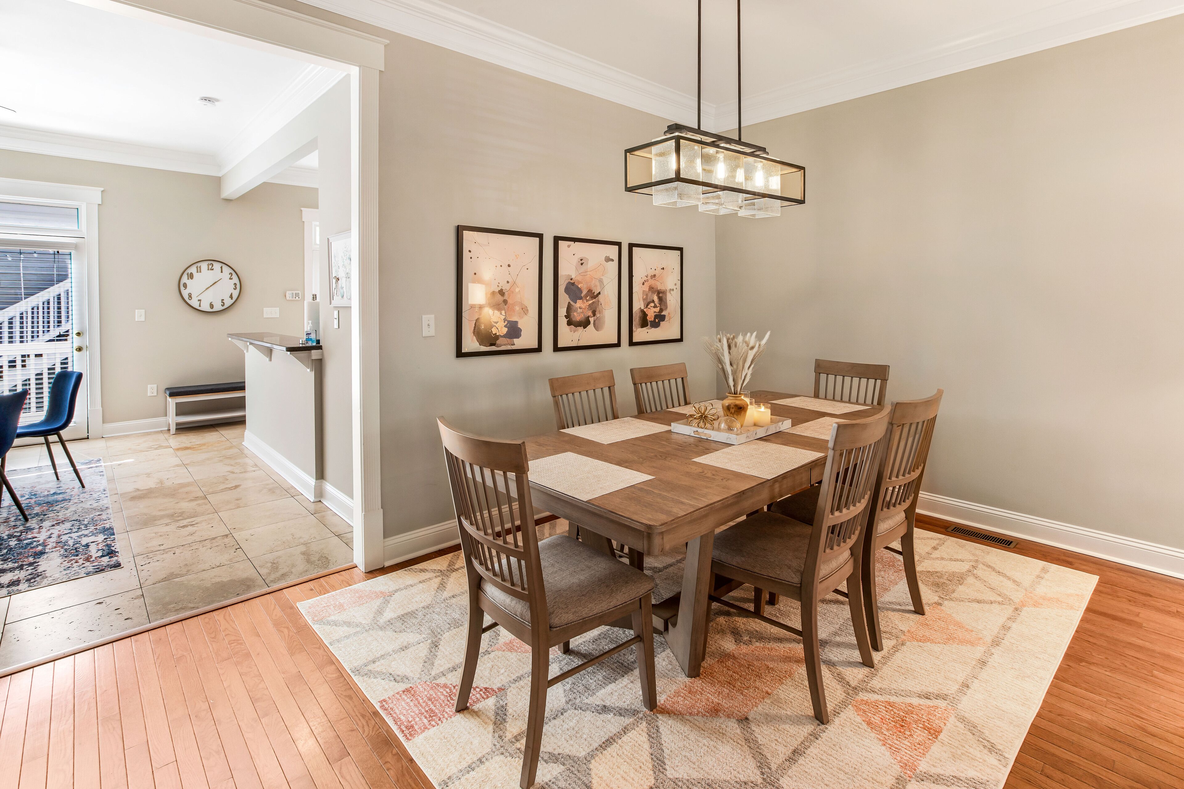 Un coin repas comprenant une table en bois, six chaises, un lustre et trois tableaux abstraits accrochés au mur.