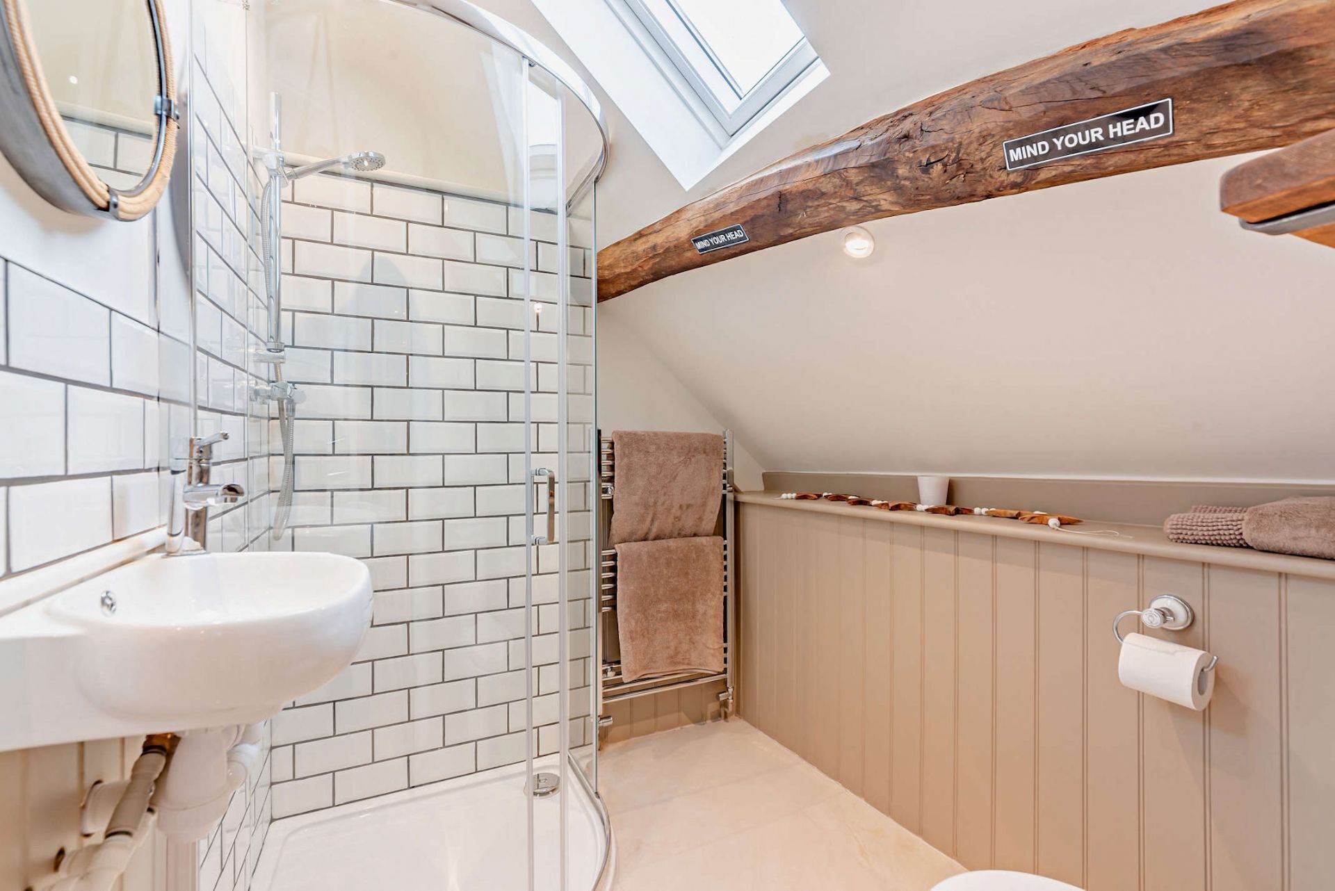 Une salle de bain moderne avec une douche à parois de verre, un lavabo blanc et une poutre en bois au plafond.