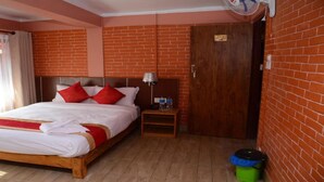 Habitación de hotel con cama de madera, almohadas rojas, una mesita de noche, un ventilador y una pared de ladrillo.
