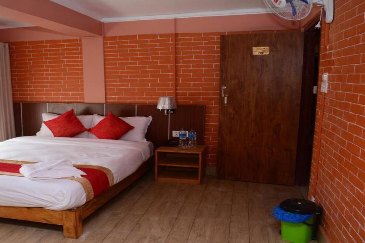 A hotel room with a wooden bed, red pillows, a nightstand, a fan, and a brick wall.