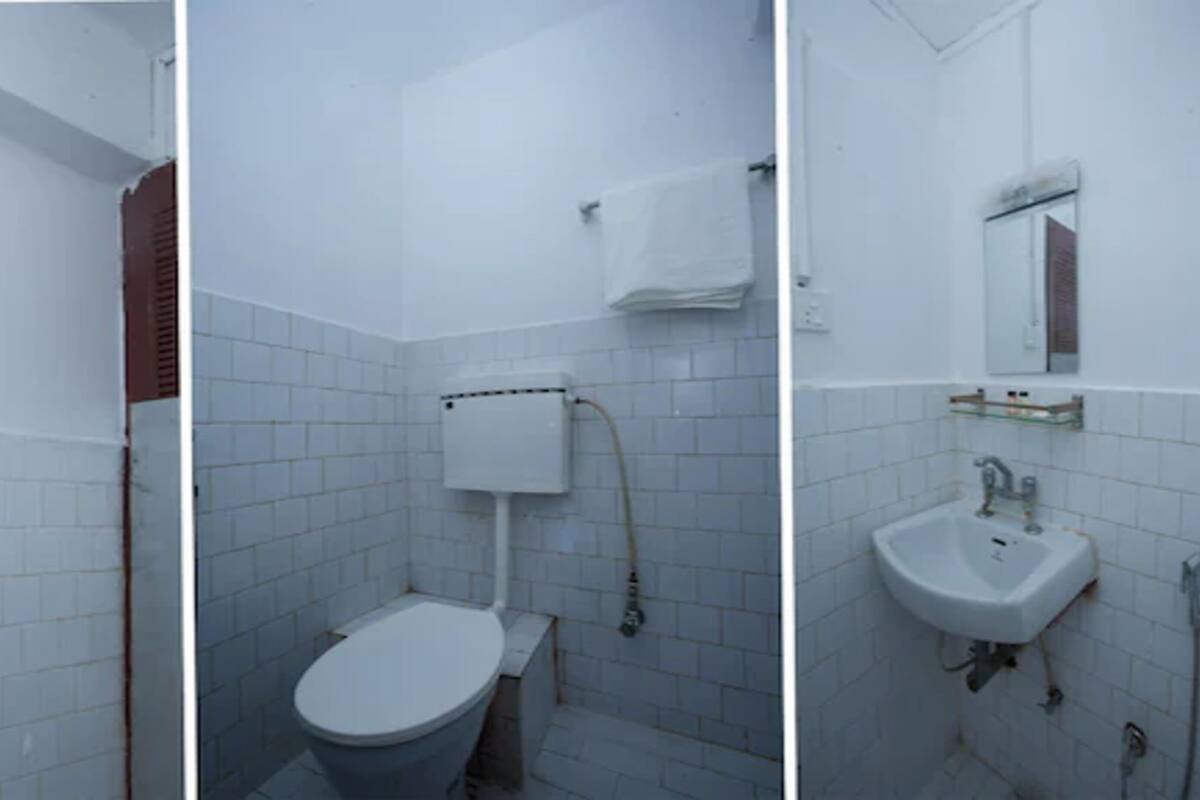 A bathroom with white tiled walls, a toilet, a sink, and a shower area.