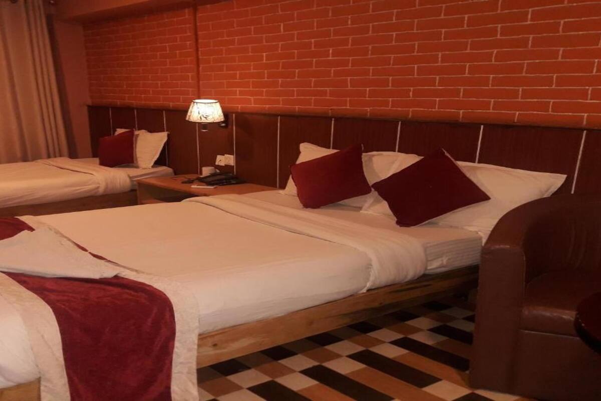 A hotel room with two beds, a checkered floor, a brick wall, and a nightstand with a lamp.
