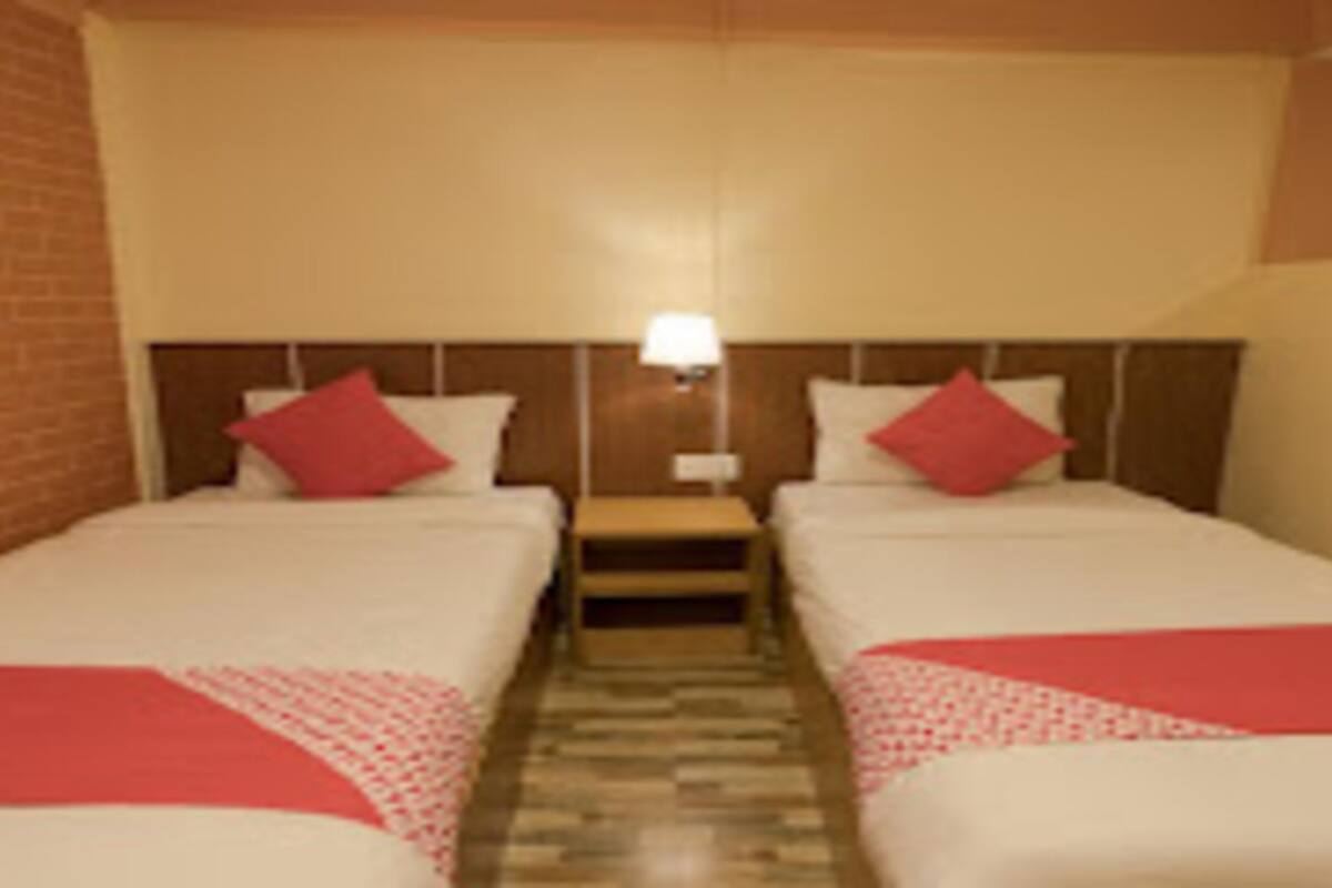 A hotel room with two single beds, each with a red blanket and pillow, a wooden headboard, and a small table between the beds.