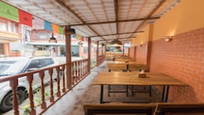 Un café al aire libre con mesas y bancos de madera, un muro de ladrillo en un lateral, y un coche estacionado fuera.