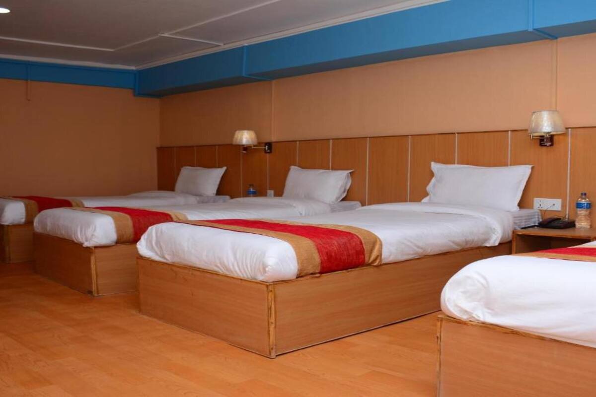 A hotel room with three single beds, wooden headboards, and bedside lamps.