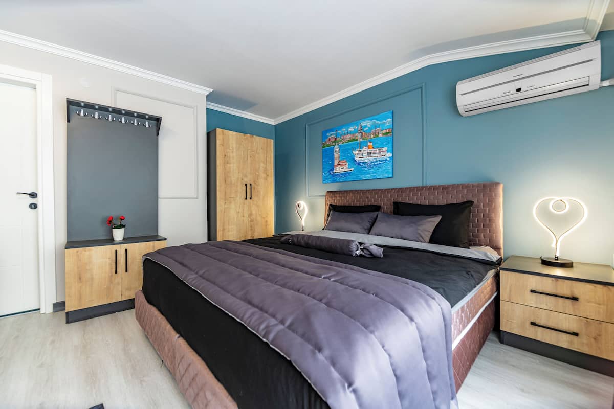 A bedroom with a large bed, a wardrobe, a nightstand, and a wall-mounted air conditioner.