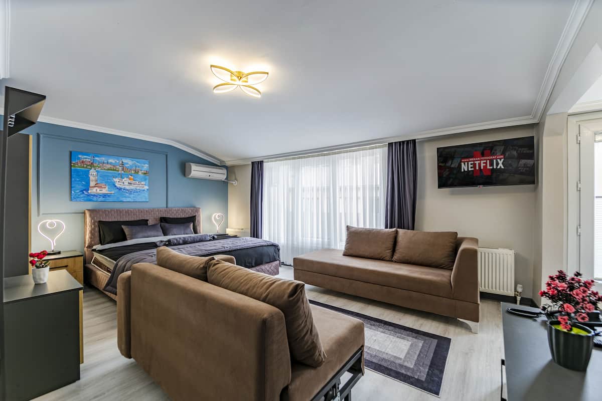 A modern hotel room with a bed, sofa, and a TV displaying the Netflix logo.