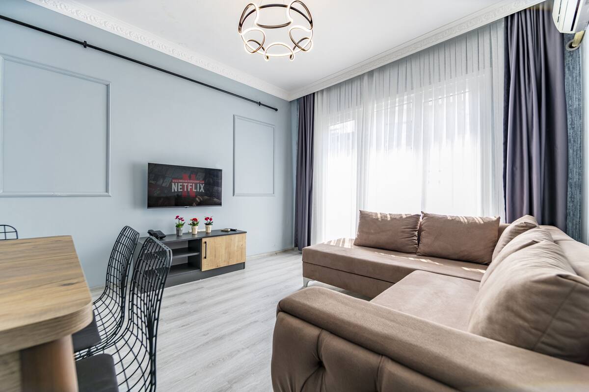 A modern living room with a sofa, a TV mounted on the wall, and a dining area with a table and chairs.