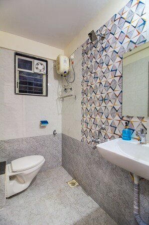 A bathroom with a toilet, sink, and a window with a fan. - Opal Suite Rooms (Pune)