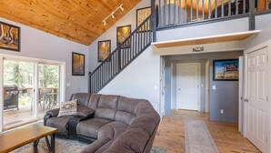 A spacious living room with a large sectional sofa, a wooden coffee table, and a staircase leading to an upper level. - Hot Tub, Secluded, Borders National Forest, New AC (Pagosa Springs)