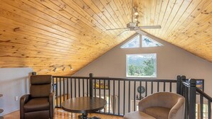 A cozy loft bedroom with a sloped ceiling, a large window, a ceiling fan, and a view of the outdoors. - Hot Tub, Secluded, Borders National Forest, New AC (Pagosa Springs)
