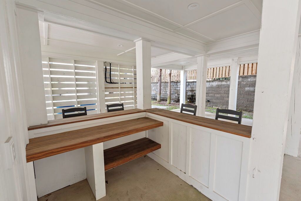 A room with a wooden bench, white paneled walls, and a view of a brick wall outside.