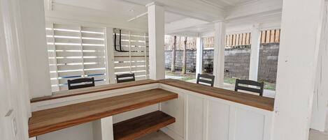 A room with a wooden bench, white paneled walls, and a view of a brick wall outside.