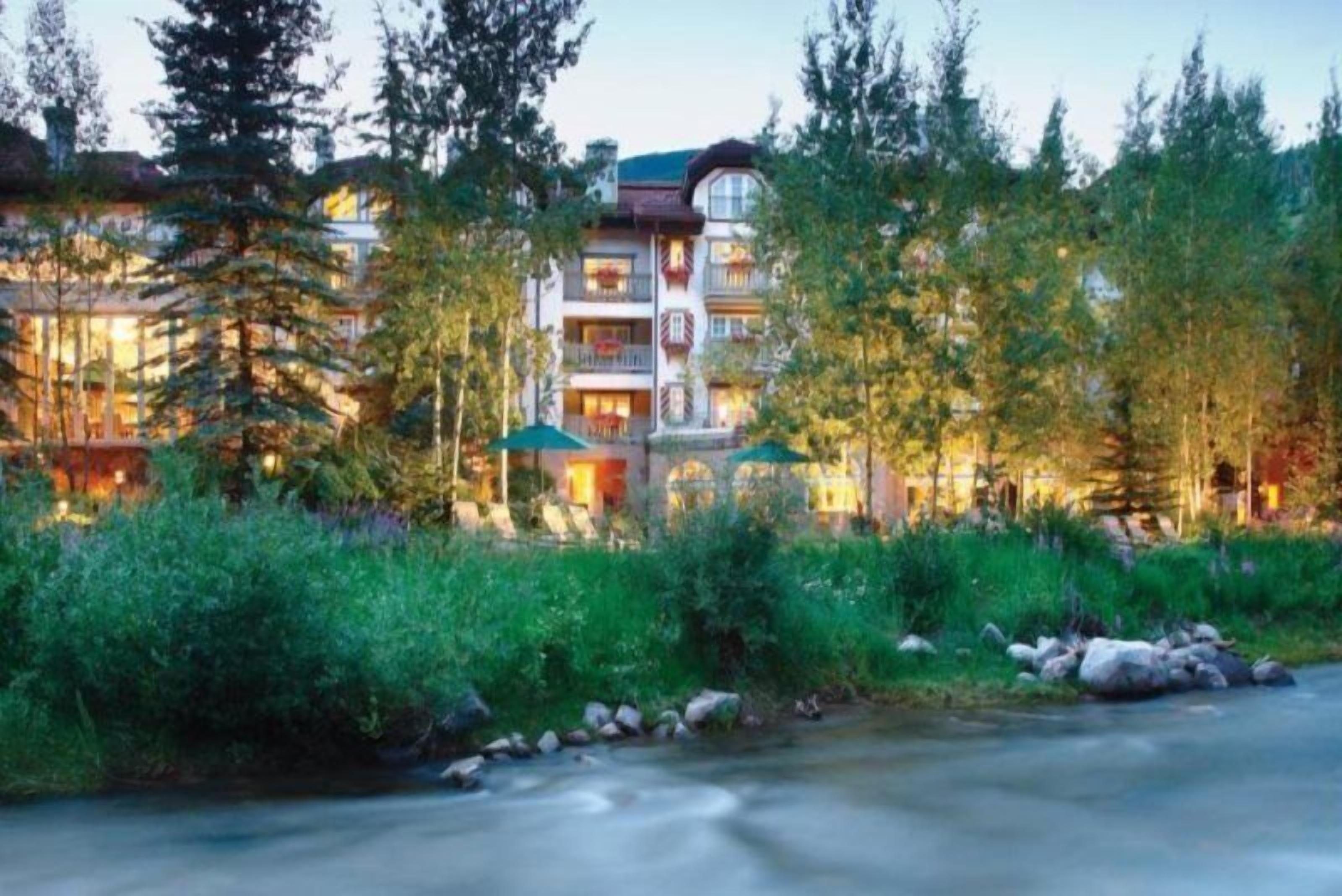 Ein mehrstöckiges Hotel mit Balkonen, umgeben von dichtem Wald und einem Bach.
