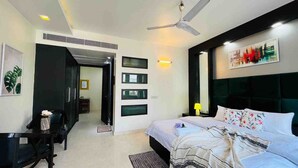 A modern hotel room with a bed, a desk, a chair, a ceiling fan, and a wall-mounted artwork.