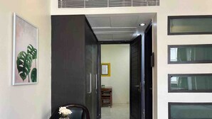 A hallway with a dark-colored wardrobe, a framed plant, a small table with a vase, and a door leading to another room.