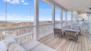A covered outdoor deck with a wooden floor, white railings, and a view of the beach.