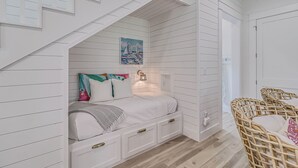Une chambre avec un plafond en pente, un lit avec une literie blanche, un tableau représentant des voiliers et un fauteuil en osier.