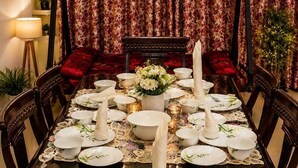 A dining table set with plates, bowls, and candles, surrounded by chairs. - Dhairya Villa Home Away From Home (Jammu)