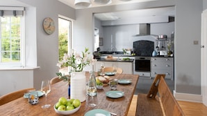 Una cocina moderna con una mesa de comedor de madera, armarios blancos y vistas al comedor contiguo.