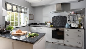Una cocina moderna con encimera de granito, armarios blancos, horno empotrado y ventana con persianas.