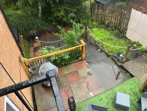 Een tuin met woonhuizen, een houten schutting, een metalen hekwerk en diverse planten.