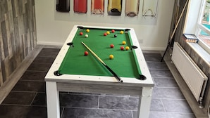 Une table de billard avec des billes, une queue de billard et un mur décoré de bouteilles.
