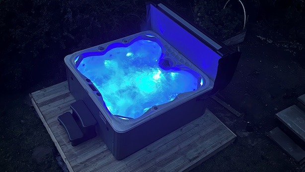 Un bain à remous avec un éclairage bleu, installé sur une terrasse en bois.