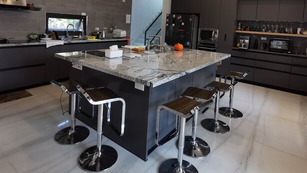 A modern kitchen with a central island, bar stools, and built-in appliances. - Dear house (Puli)