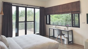 A bedroom with a bed, a desk, and a view of greenery through large windows. - Dear house (Puli)