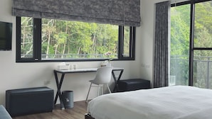 A modern bedroom with a large bed, a desk with a chair, a small trash bin, and a TV mounted on the wall. - Dear house (Puli)