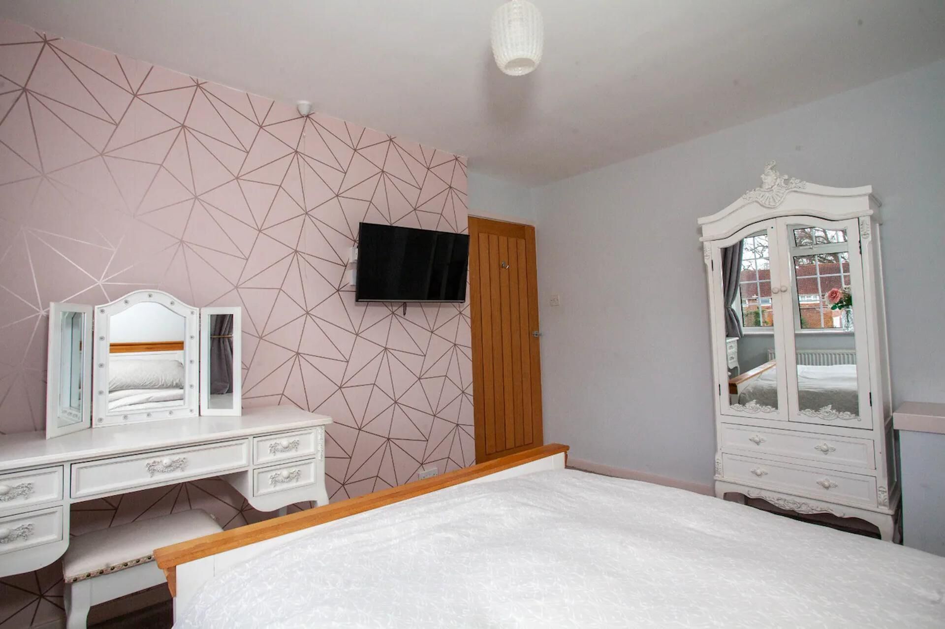 A bedroom with a bed, a dresser, a vanity, a television, and a wardrobe.